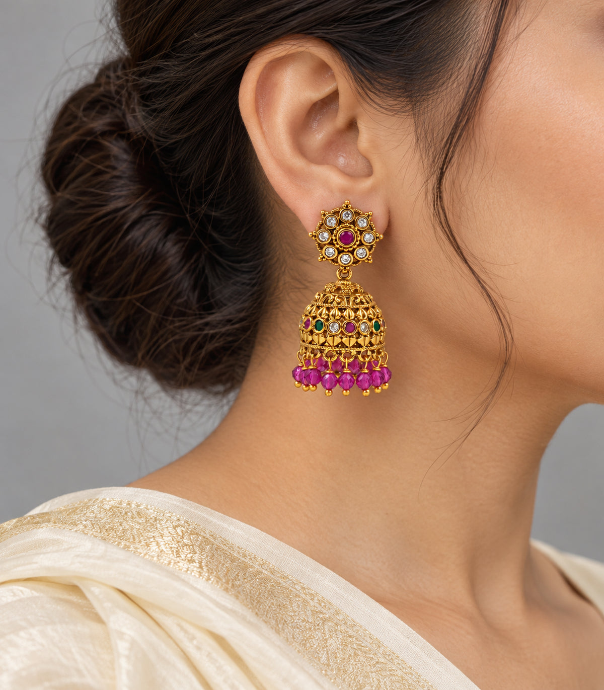 Gold-tone magenta and green jhumka earring worn with an ivory sari