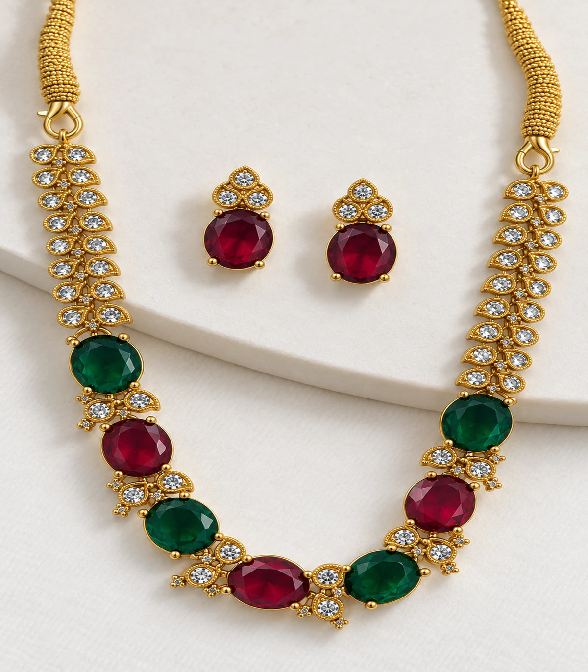 Close detail of the magenta and green oval necklace and matching earrings on a pale surface