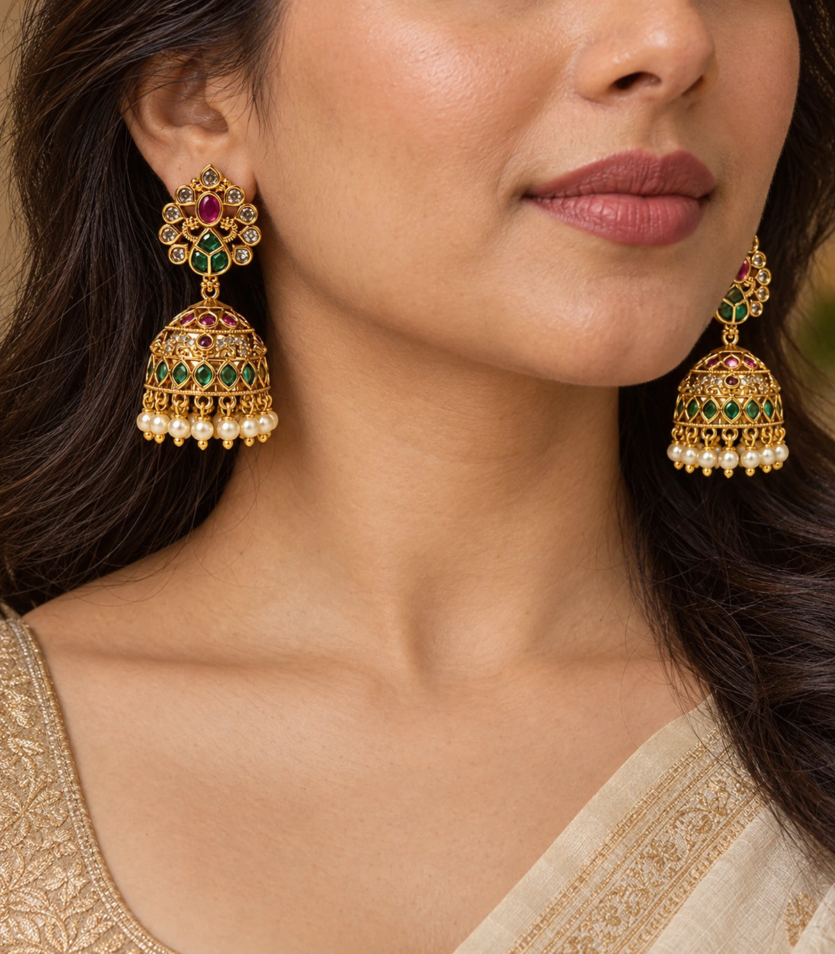 Closeup of worn peacock jhumka earrings showing magenta tops, green bell panels and pearl-like drops