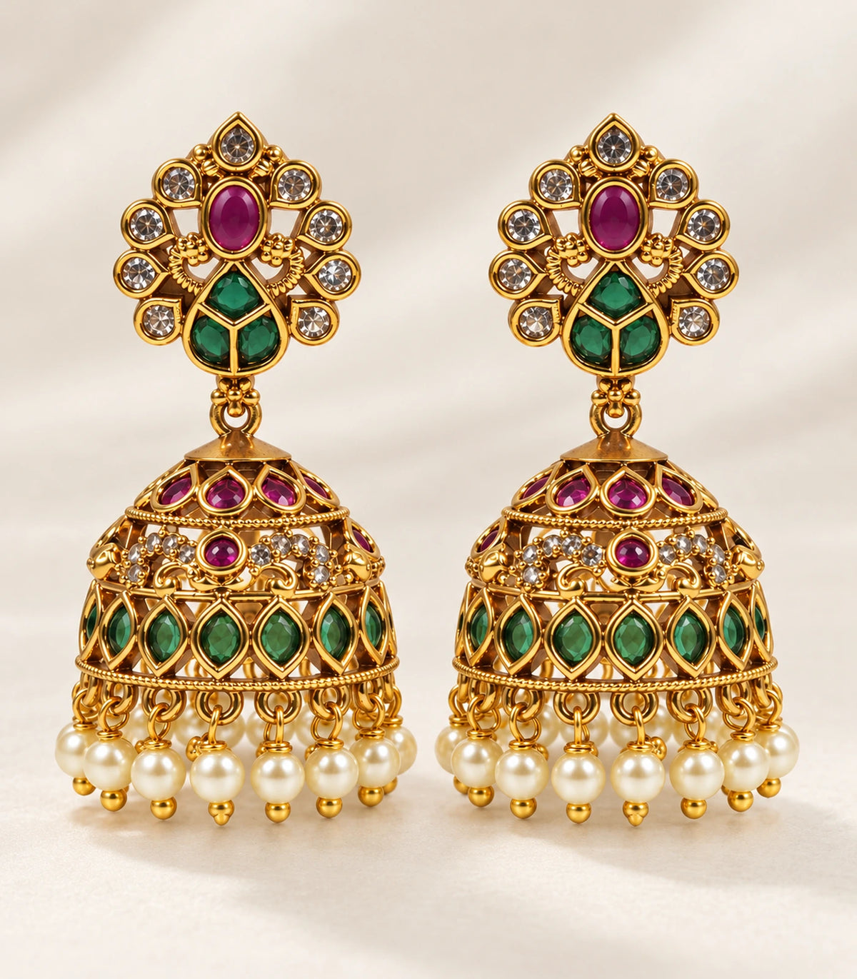 Matching pair of gold-tone peacock jhumka earrings arranged on a neutral surface