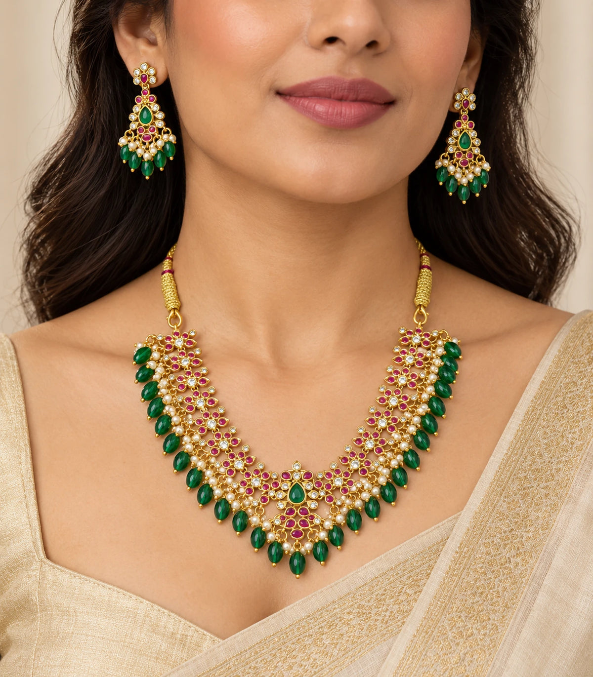 Gold-tone magenta and green necklace and matching earrings worn with a cream outfit