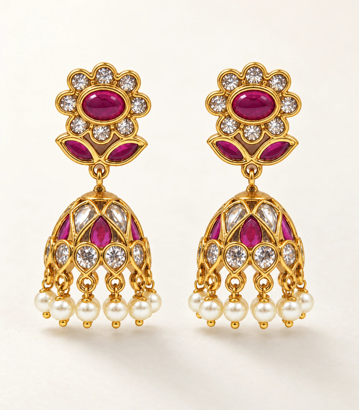 Full pair of gold magenta floral jhumka earrings arranged on a neutral surface
