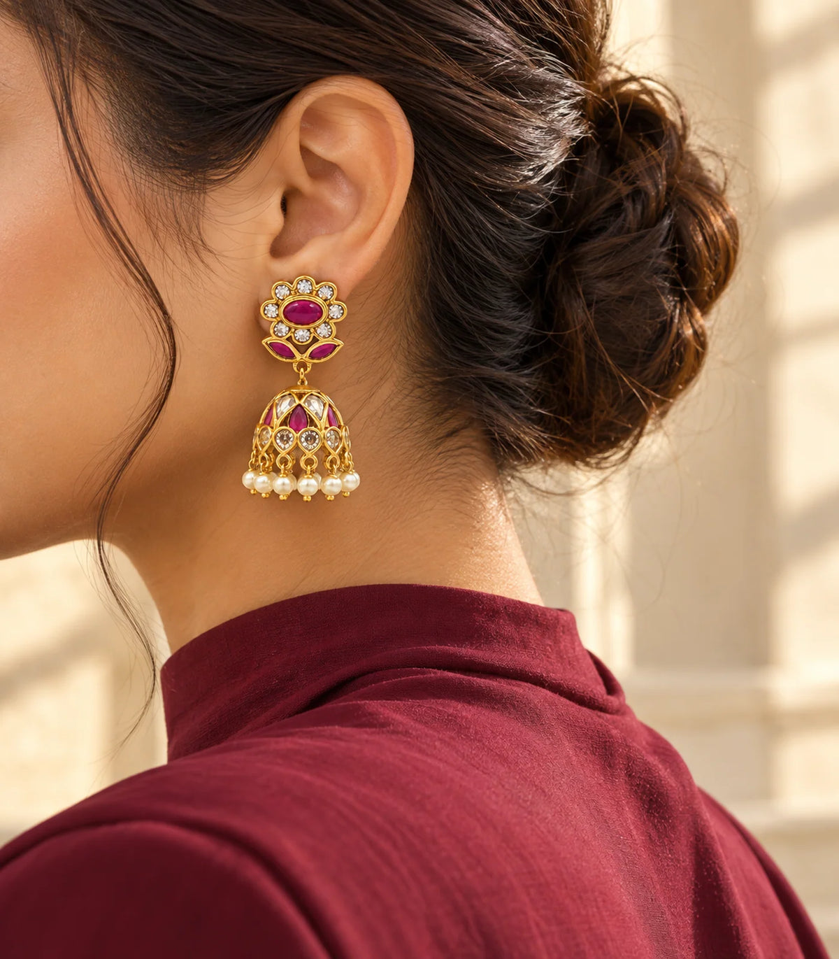 Gold magenta floral jhumka earrings worn with an embroidered outfit in an editorial pose