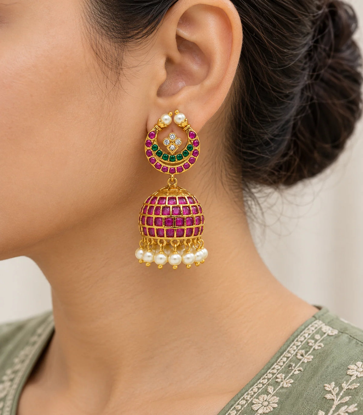 Close view of magenta and green stone detailing and white pearl-like drops on worn gold-tone jhumka earrings