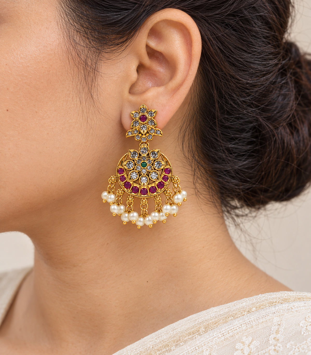 Close-up of the floral stud, circular drop and pearl fringe of the gold, magenta and green chandbali earring