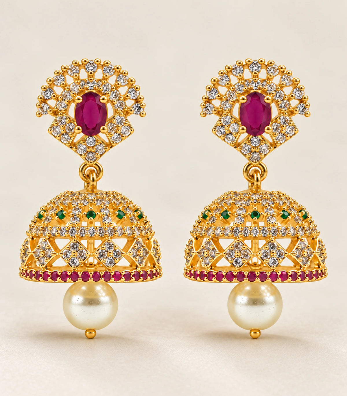 Complete matching pair of gold-tone magenta and green floral pearl jhumka earrings on a neutral surface