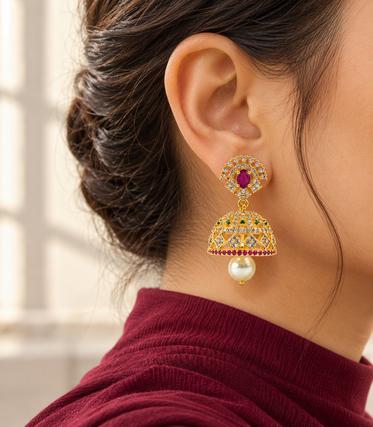 Gold-tone magenta and green floral pearl jhumka earring worn with a burgundy high neckline