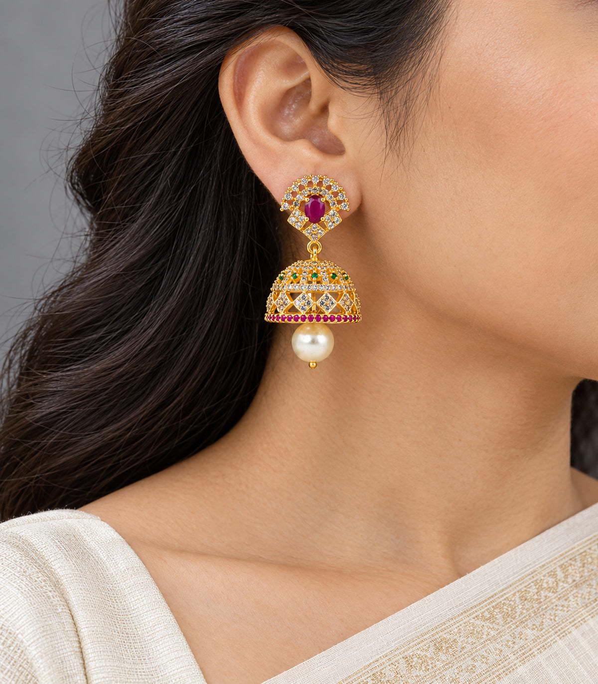 Gold-tone magenta and green floral pearl jhumka earring worn in an ivory sari side view