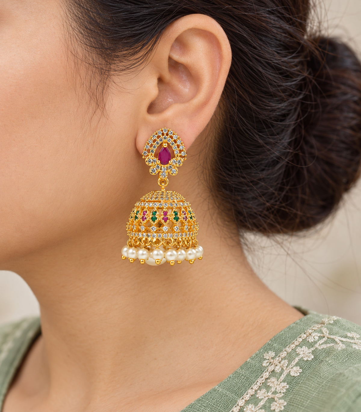 Close view of a worn jhumka earring showing the magenta teardrop, green and magenta dome panels and white pearl-look fringe