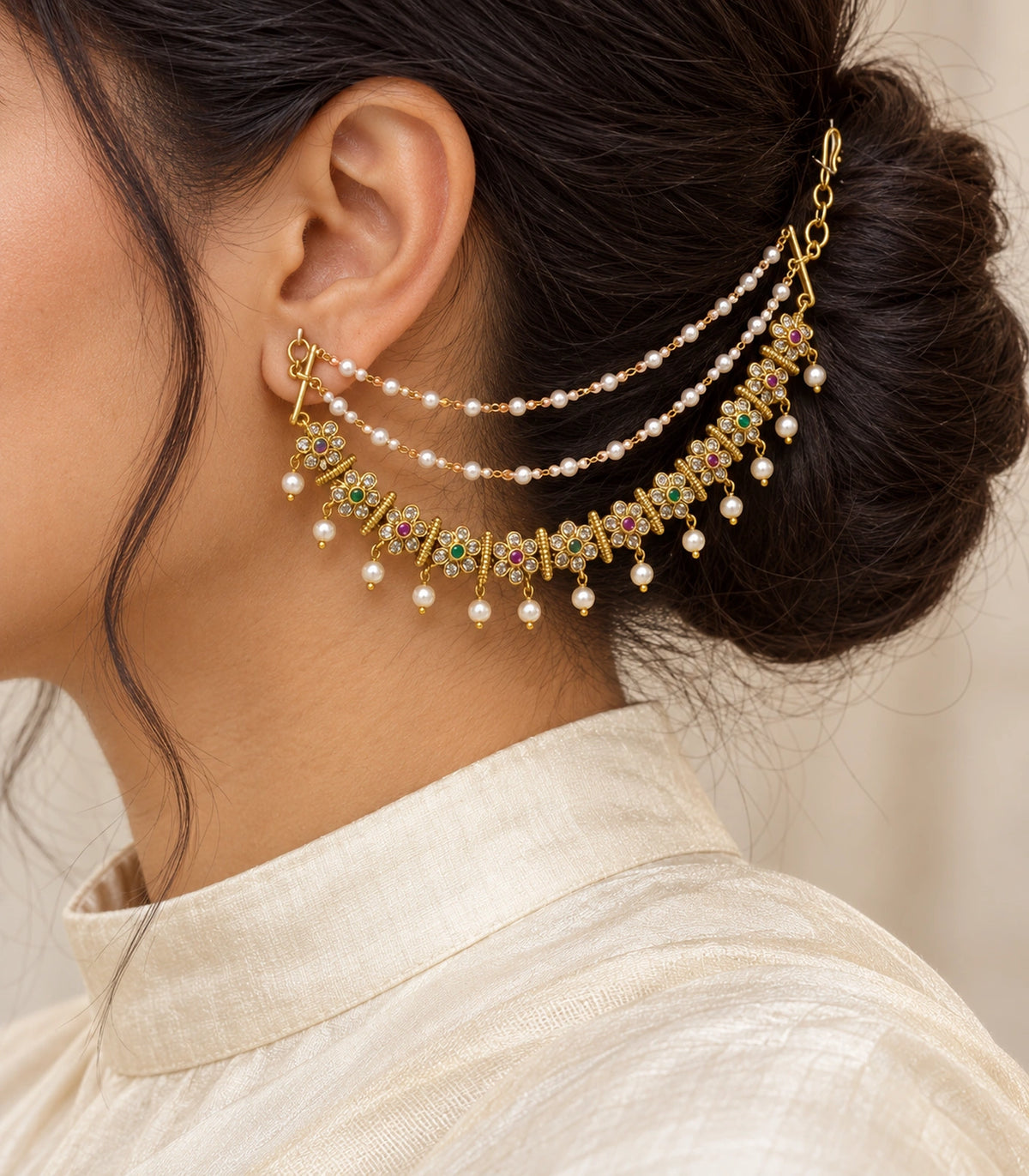 Close view of gold tone magenta and green floral pearl ear chain worn with an ivory silk collar