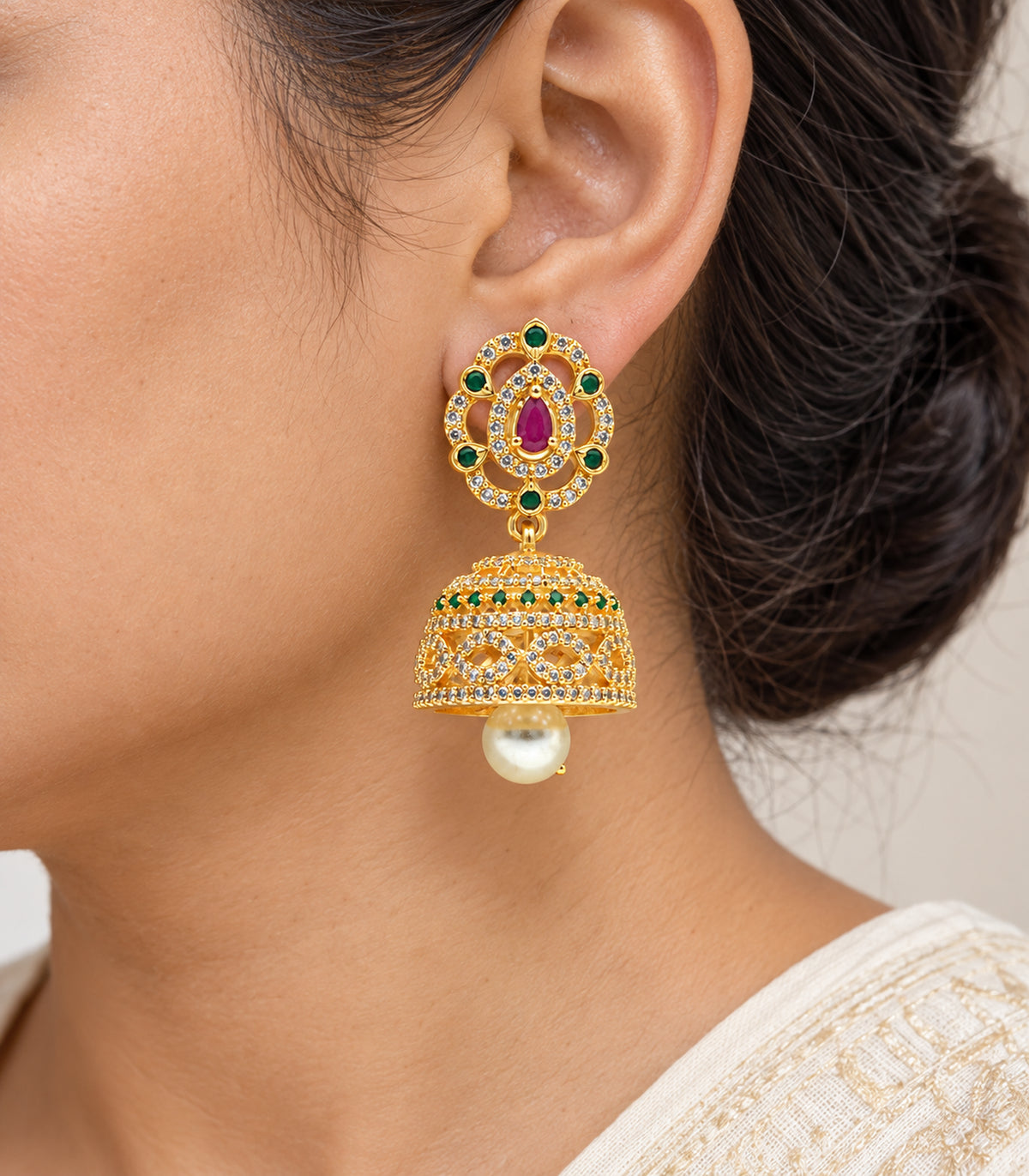 Close detail of one worn gold-tone magenta and green jhumka earring with pearl drop