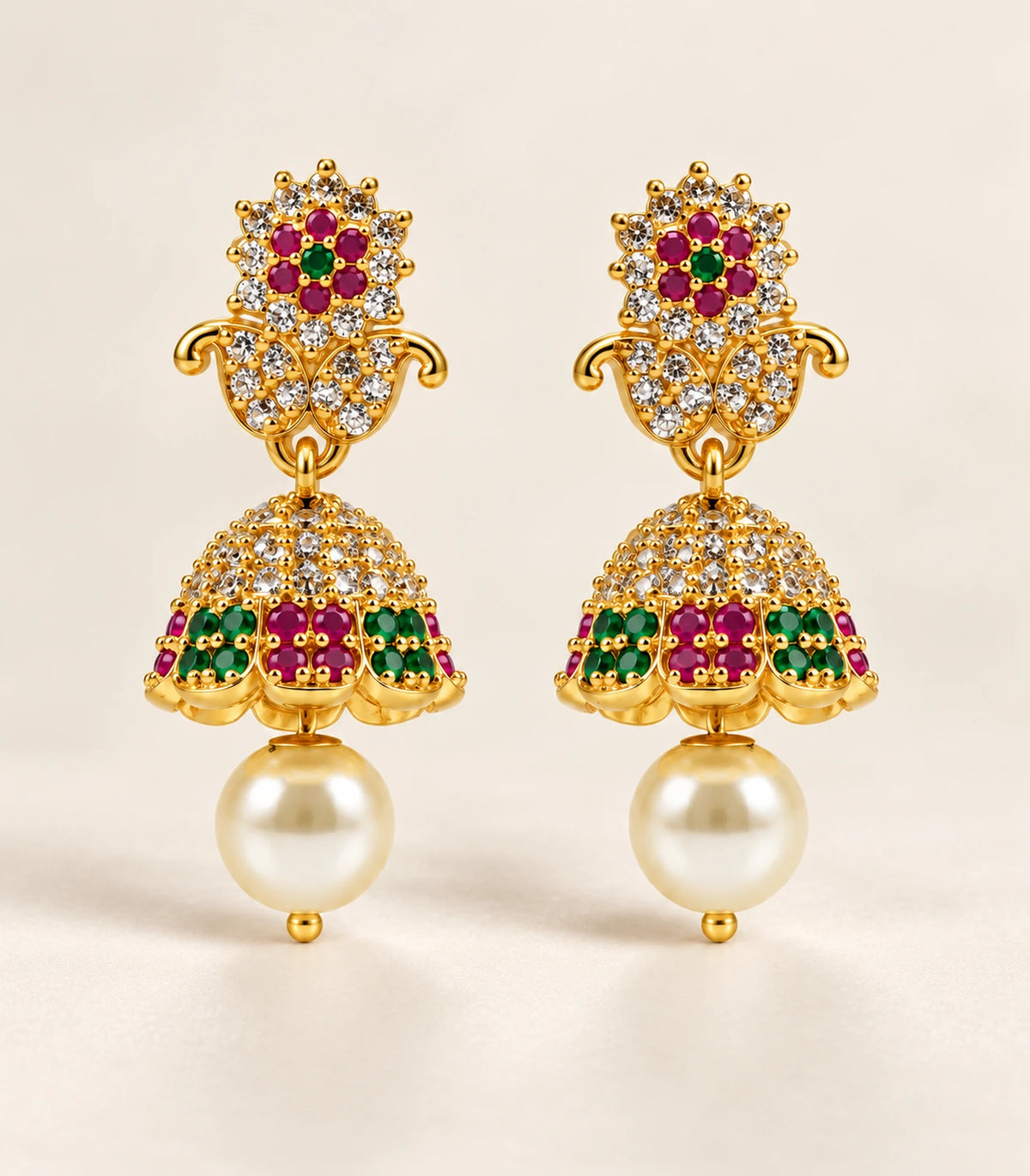Complete pair of gold-tone magenta and green earrings with cream pearl-like drops on a cream surface