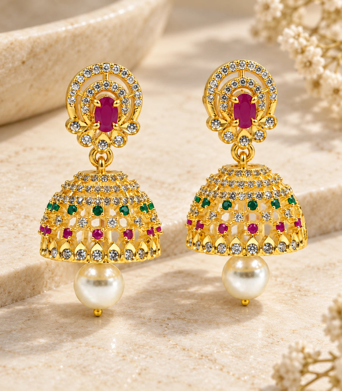 Pair of gold-tone multicolor jhumka earrings displayed on a cream stone surface