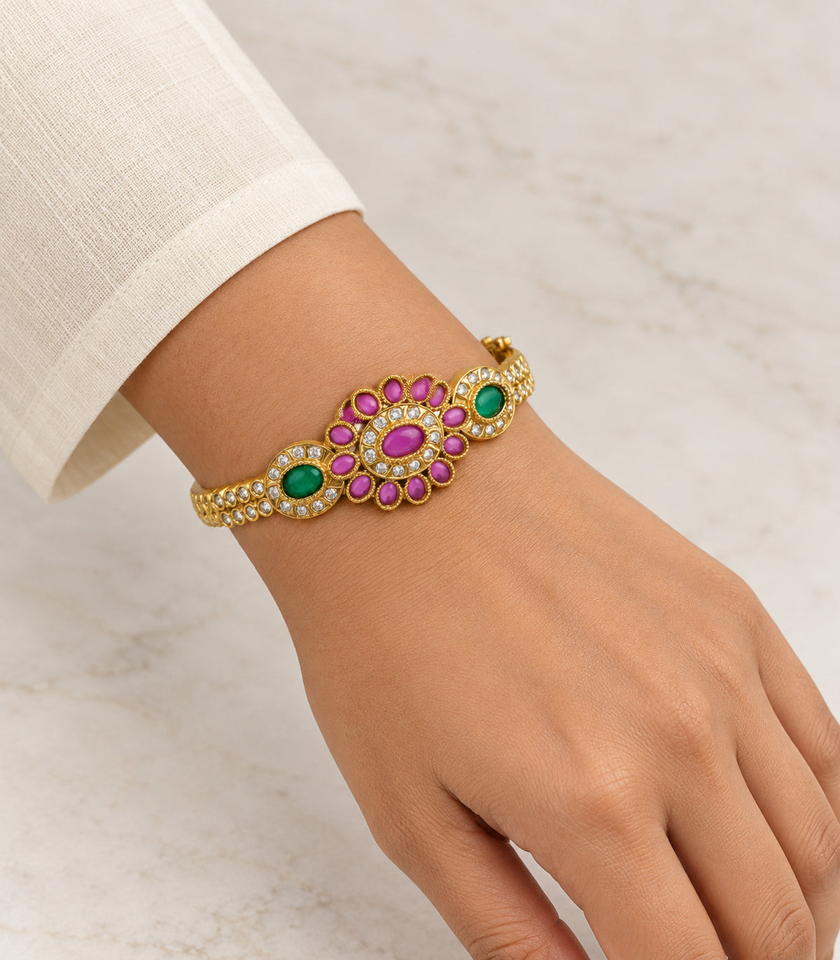 Gold magenta oval flower green halo bangle worn on a wrist with an ivory sleeve