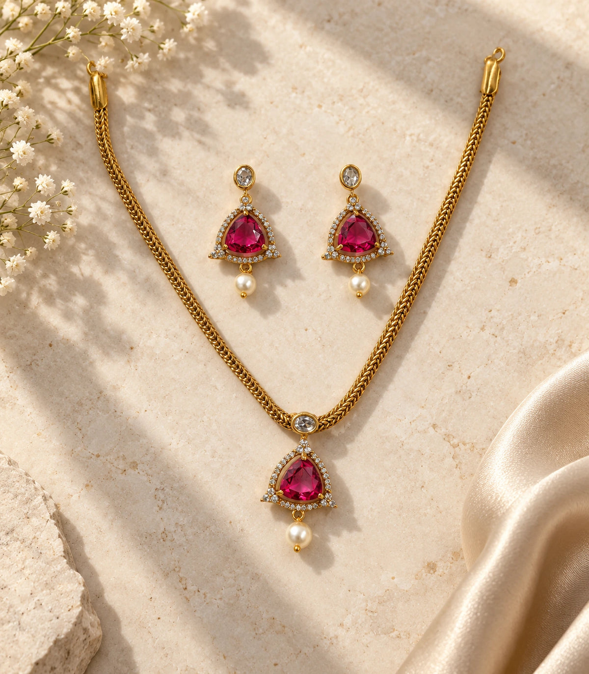 Complete gold-tone magenta necklace and earring set arranged on neutral stone