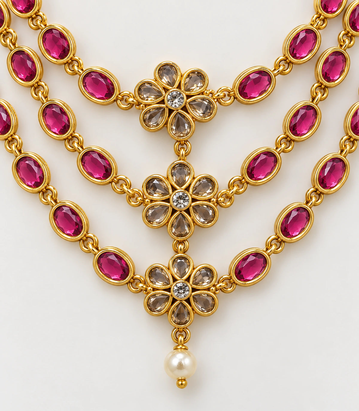Closeup of magenta oval settings, clear floral accents and the necklace's pearl-like drop