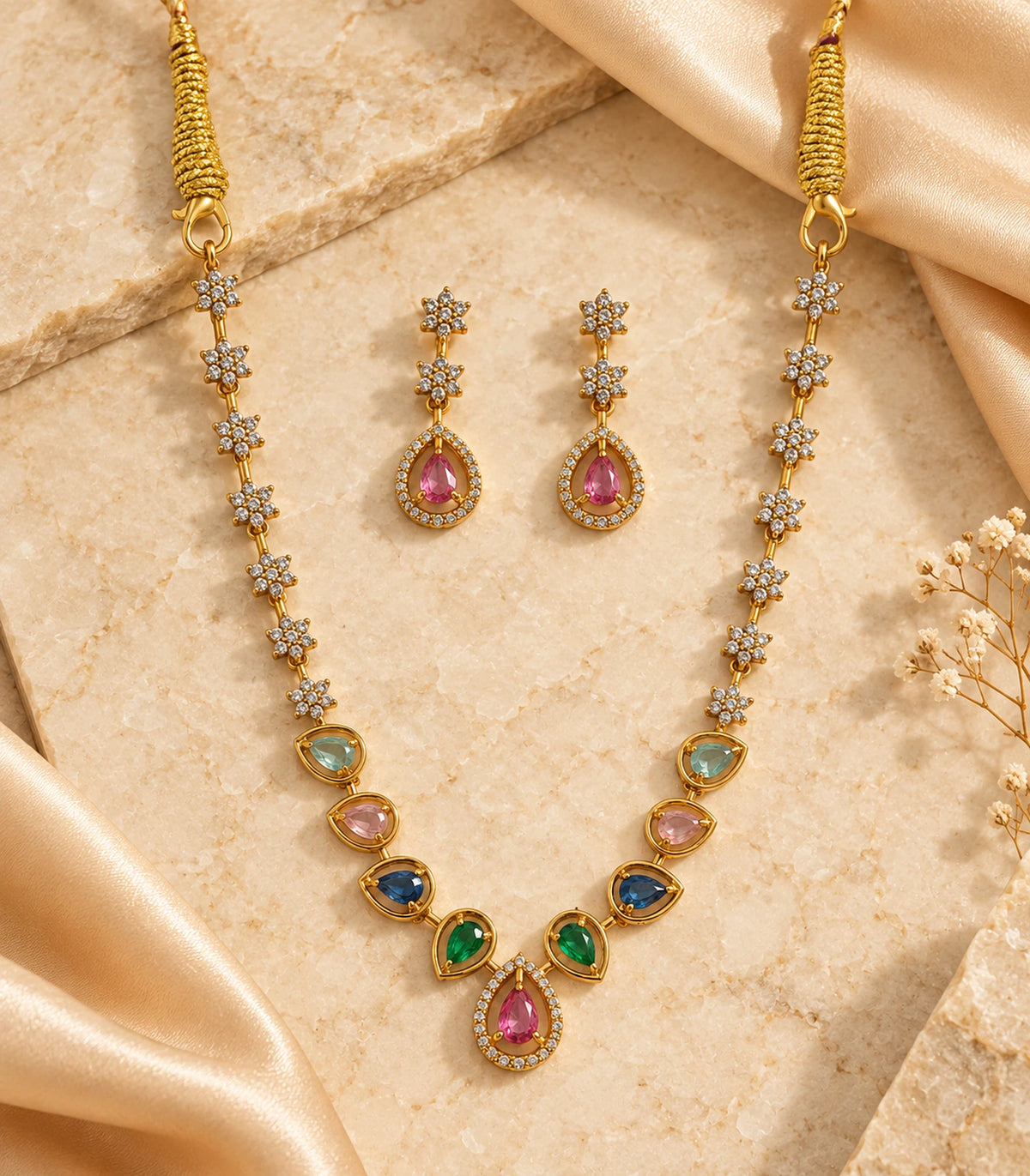 Gold-tone multicolour necklace and matching earrings arranged on stone with cream fabric