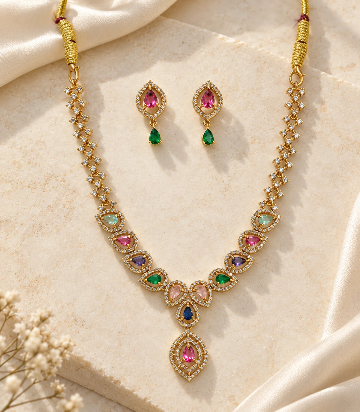 Gold-tone multicolor necklace and matching pink and green earring pair styled on a pale surface