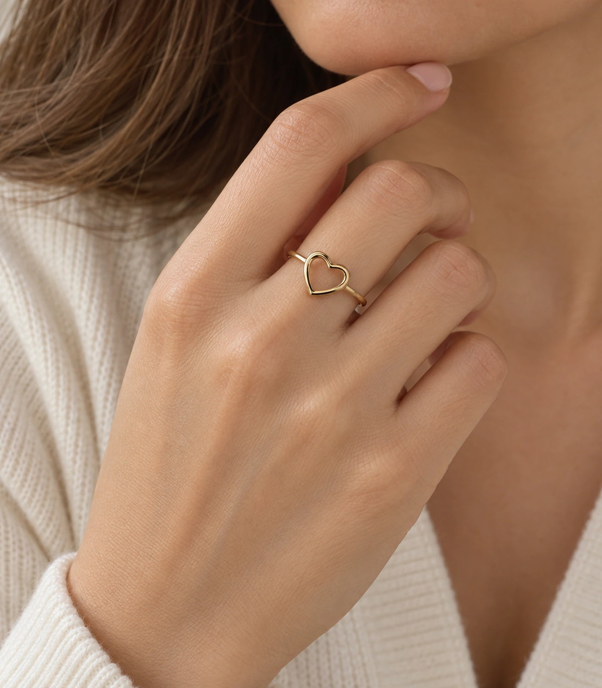 Gold open heart ring worn on a hand near the chin