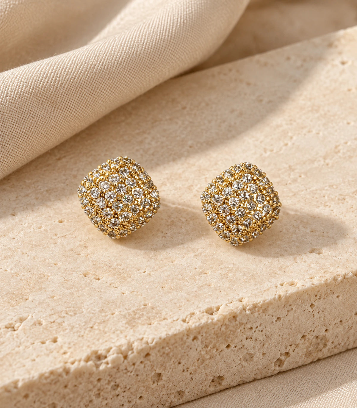Matching gold-tone cushion cluster stud earrings styled on stone and fabric