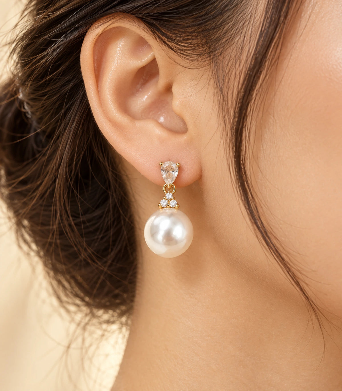 Editorial worn view of a gold-tone pear-shaped crystal-style and large white pearl-style drop earring.