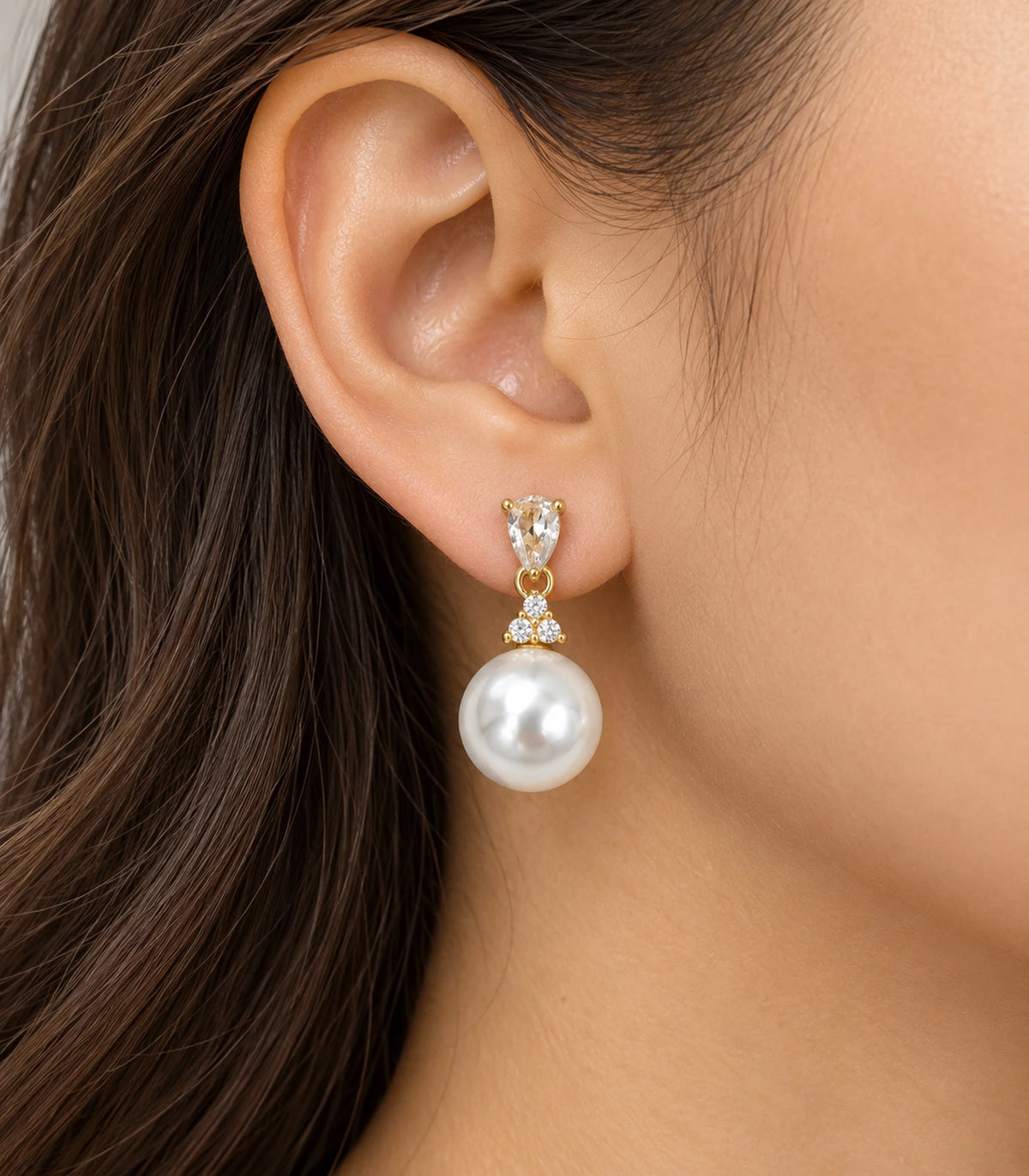 Gold-tone pear-shaped crystal-style and large white pearl-style drop earring worn at the ear.