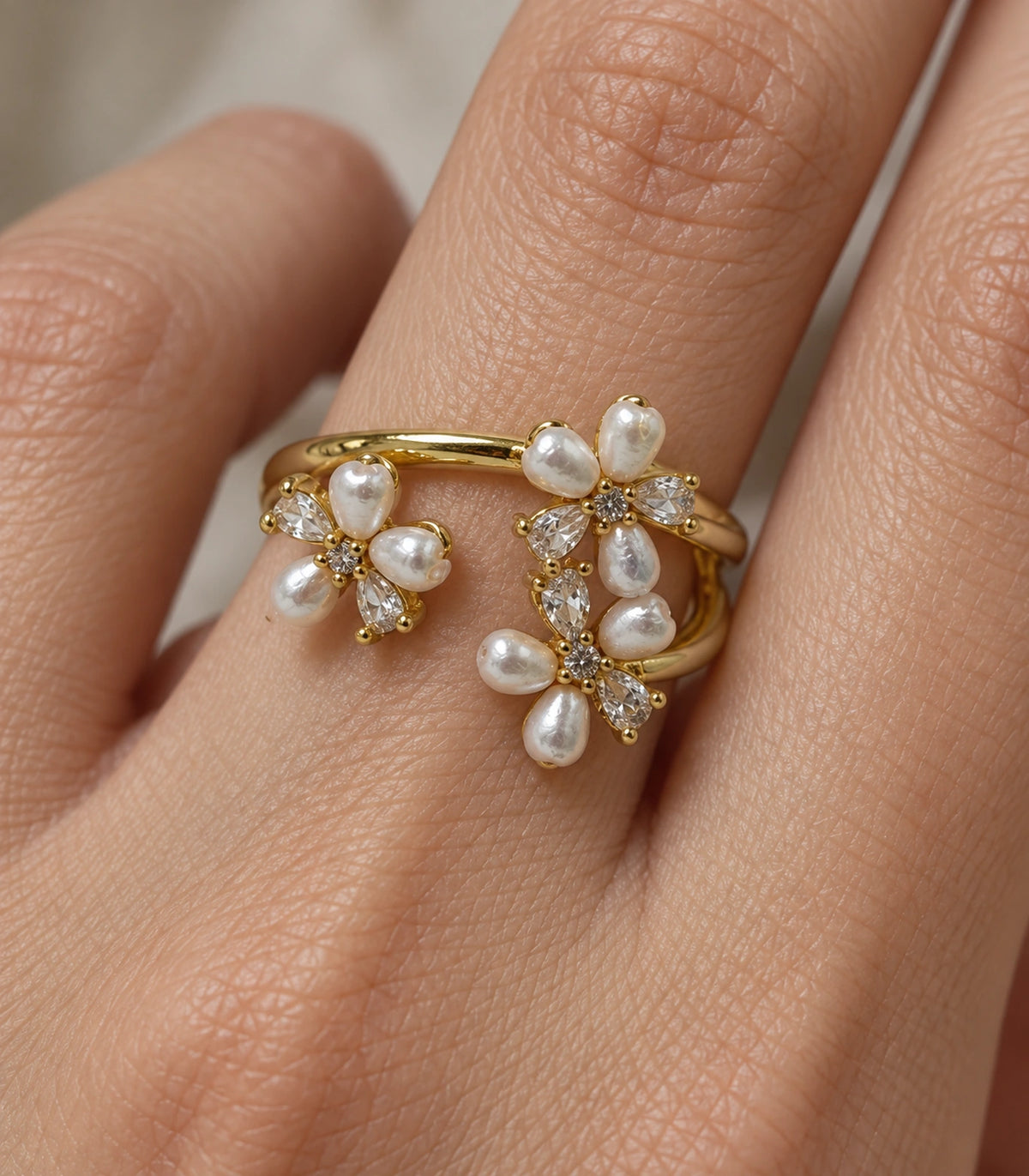 Closeup of the ring’s three floral clusters and split gold-tone open band on a finger