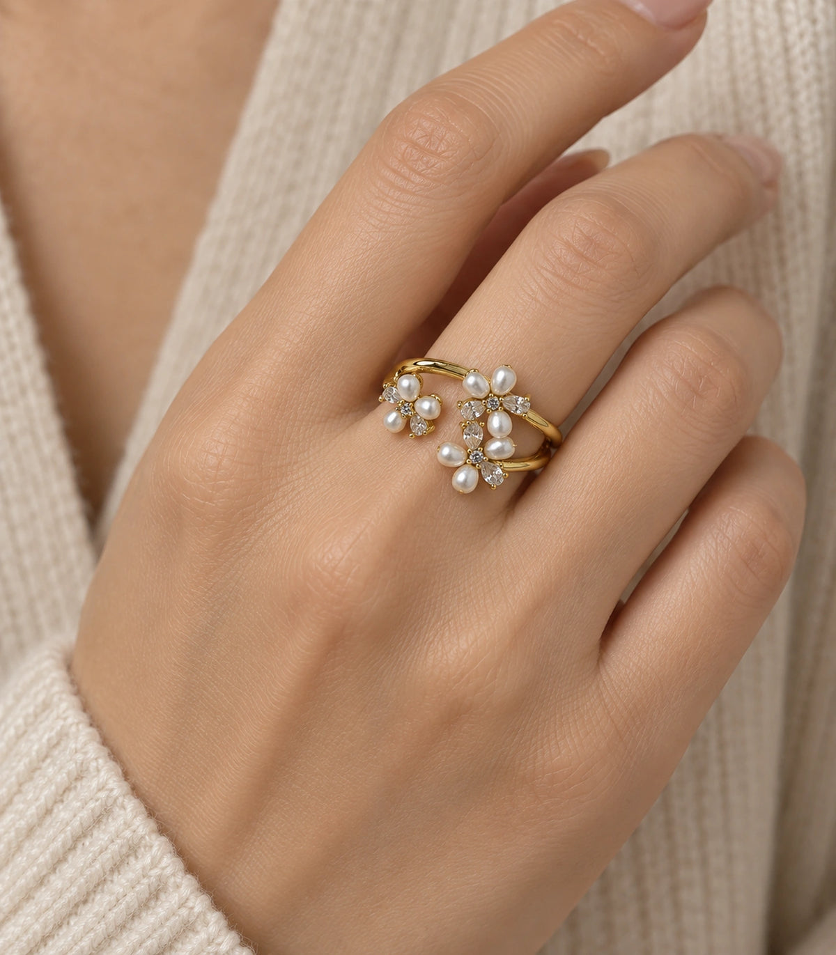 Gold pearl crystal botanical open ring worn naturally on a finger against cream knit