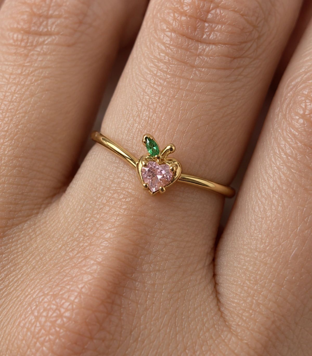 Close view of the pink heart stone, green leaf and gold-tone setting worn on a finger