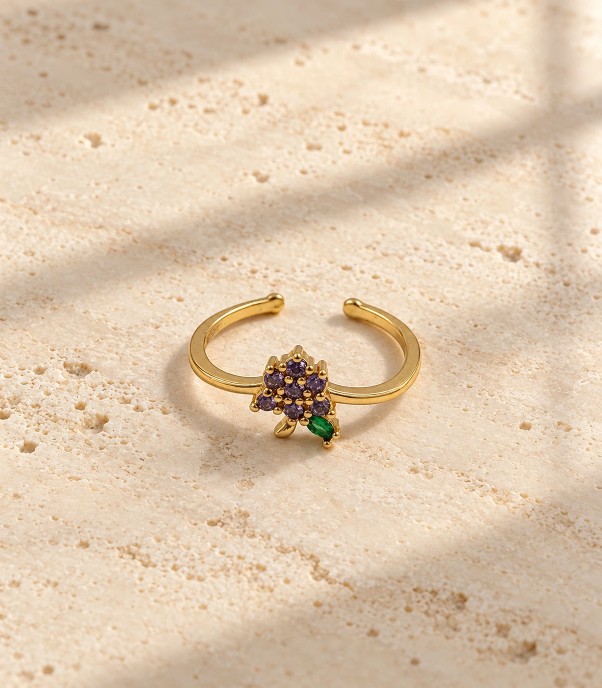 Complete gold-tone purple flower and green leaf open ring on cream stone