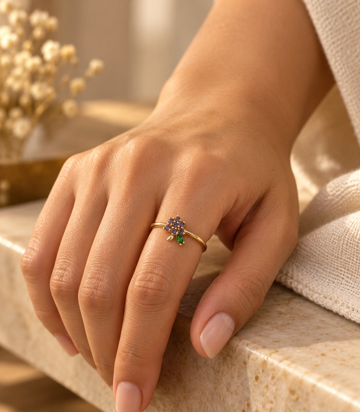 Purple flower and green leaf ring worn in a warm-lit hand composition