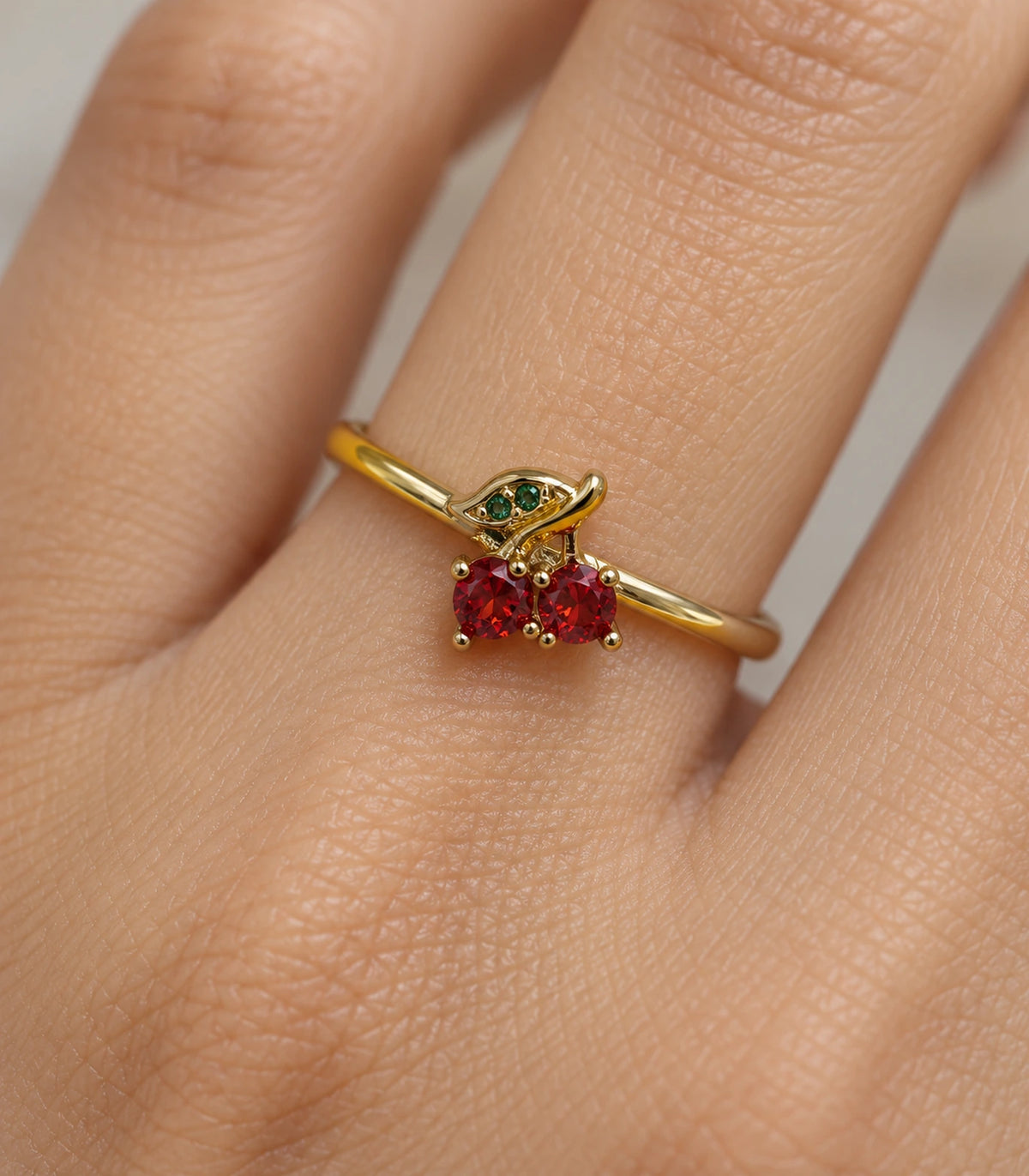 Close-up of the red cherry stones and green leaf on the worn gold-tone ring