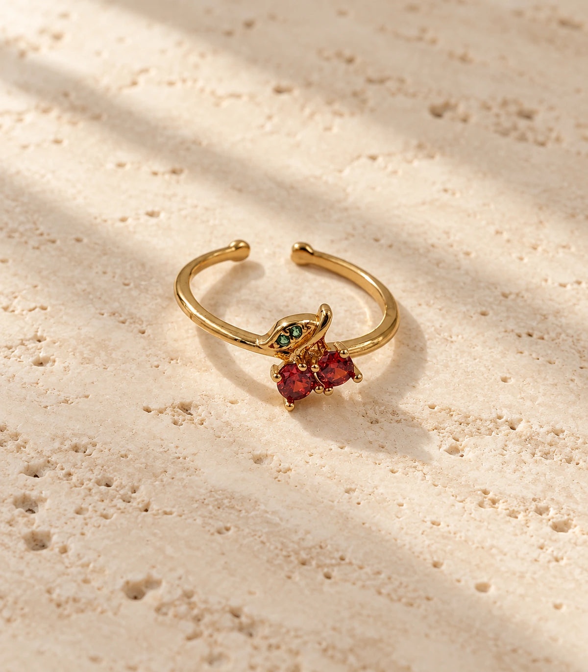 Complete gold-tone cherry open ring on a warm stone surface