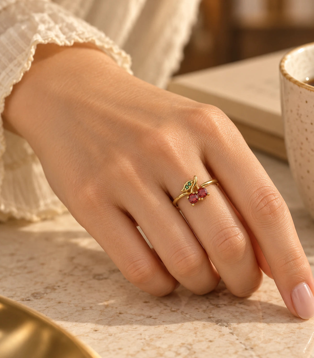 Gold-tone red cherry and green leaf ring worn in a warm tabletop setting