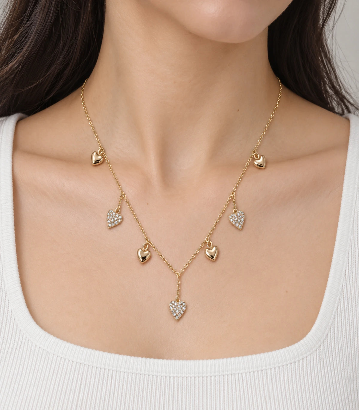 JIMIKI Gold Seven Heart Charm Necklace - worn closeup of polished and stone-set heart charms #color_gold