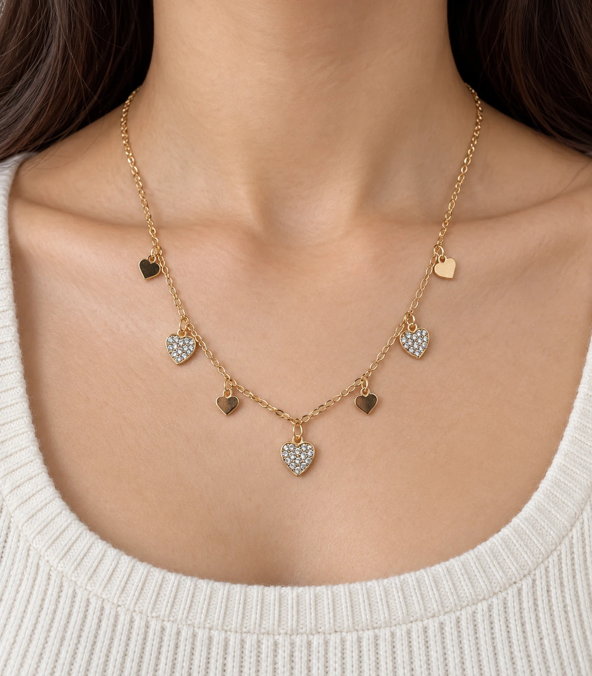 JIMIKI adjustable gold-tone seven heart charm necklace, close worn view of four plain hearts alternating with three stone-set hearts #color_gold