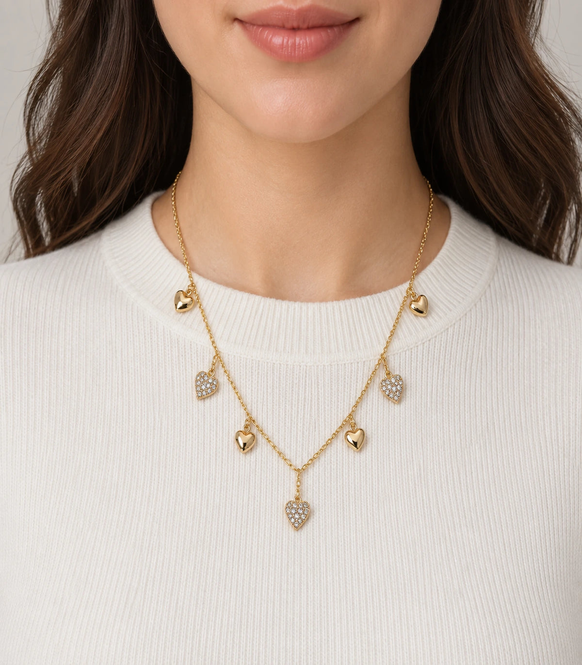 JIMIKI Gold Seven Heart Charm Necklace - seven-heart necklace worn against an ivory knit #color_gold