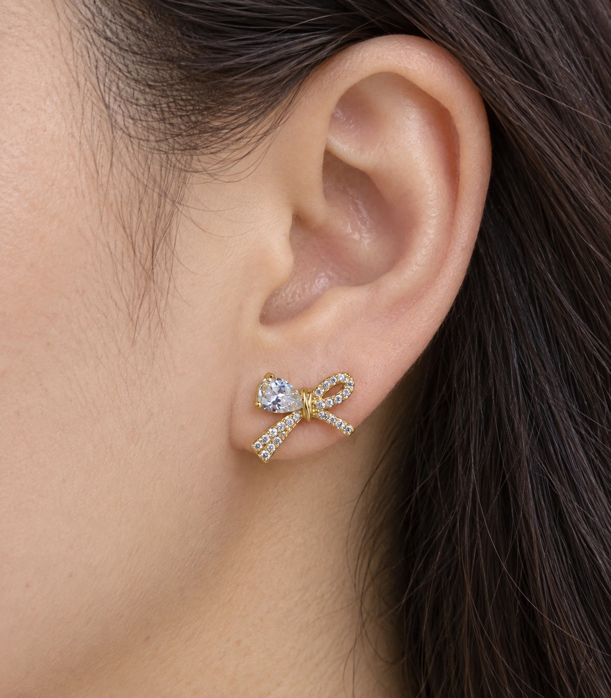 JIMIKI Gold-Tone Asymmetric Crystal Bow Stud Earrings in Gold / Clear, close-up detail