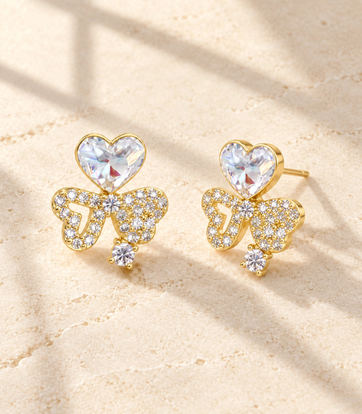 JIMIKI Gold-Tone Asymmetric Crystal Heart Bow Stud Earrings in Gold Tone, editorial flat lay