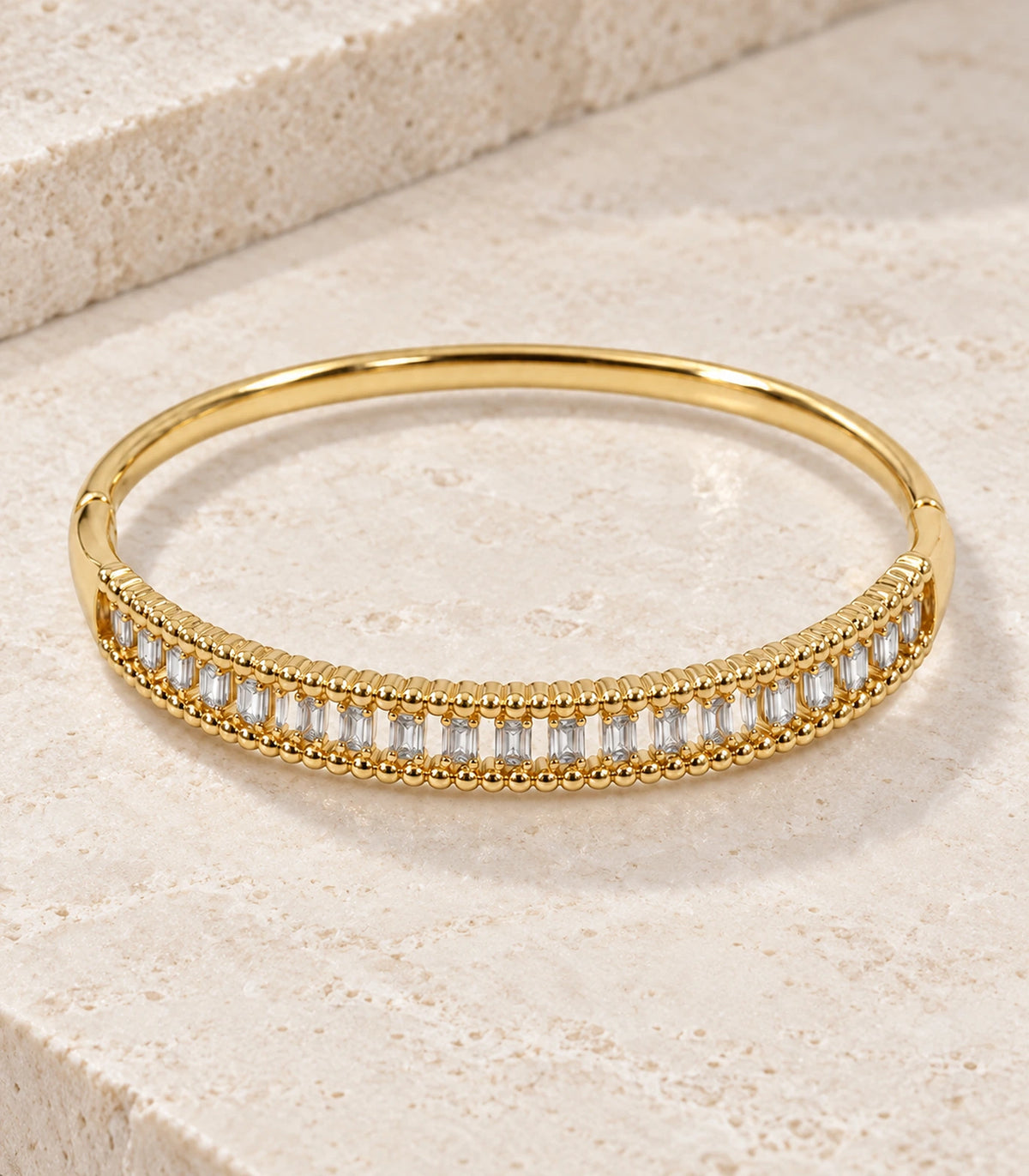 JIMIKI Gold-Tone Baguette Beaded Frame Bangle — bangle in a styled flat lay #color_gold-tone / clear