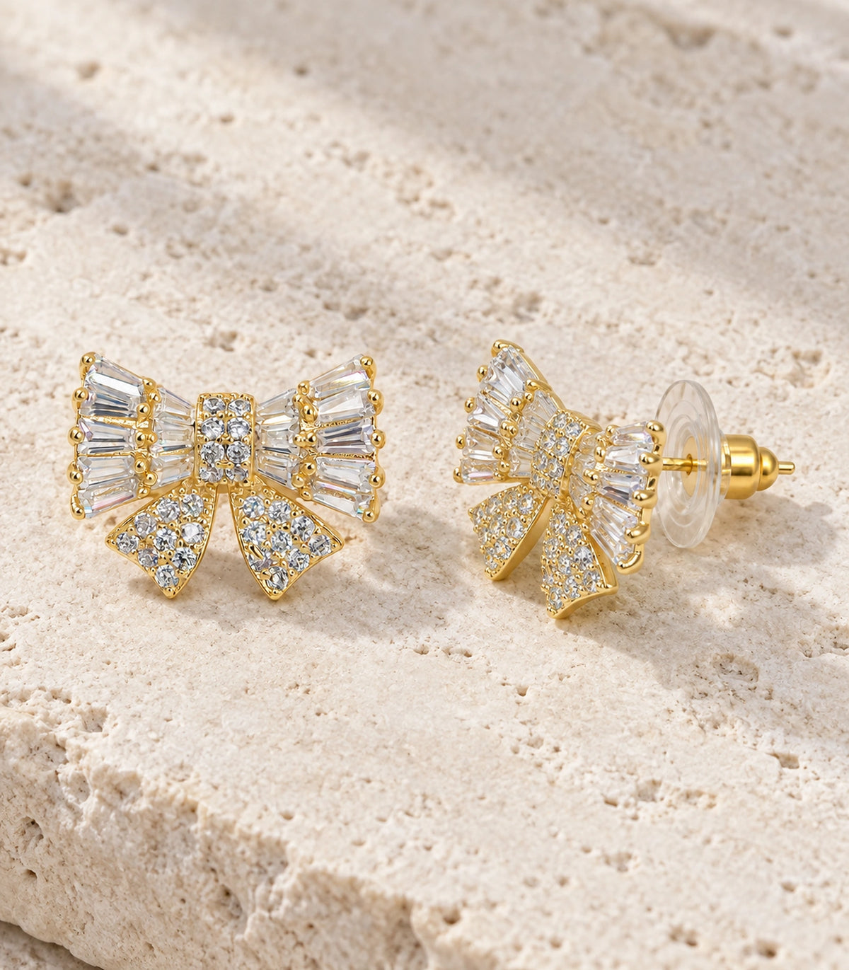 JIMIKI Baguette Crystal Bow Stud Earring Pair in Gold-tone, editorial flat lay #color_gold-tone