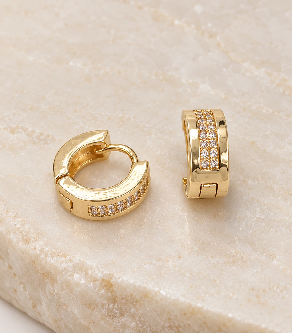 JIMIKI Gold Tone central pave strip huggie hoop earrings, pair on pale textured stone #color_gold-tone