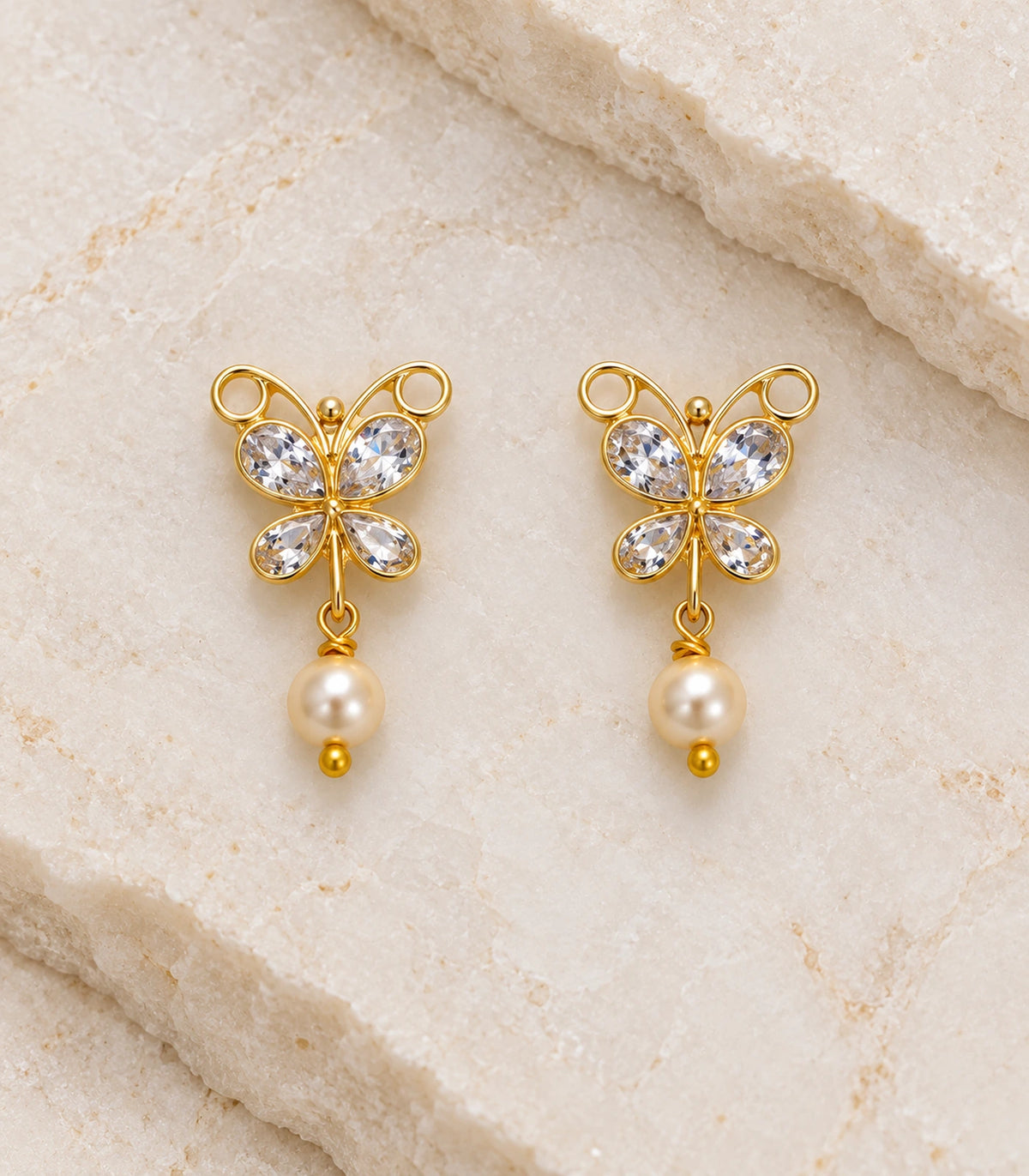 JIMIKI Clear Crystal butterfly pearl drop earrings, pair arranged on a textured surface #color_clear-crystal