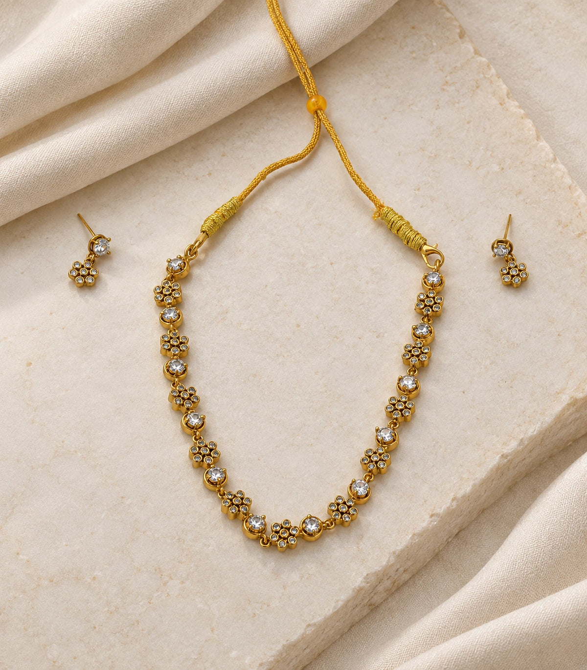 Gold-tone floral cluster necklace and matching earring pair on a light fabric and stone setting