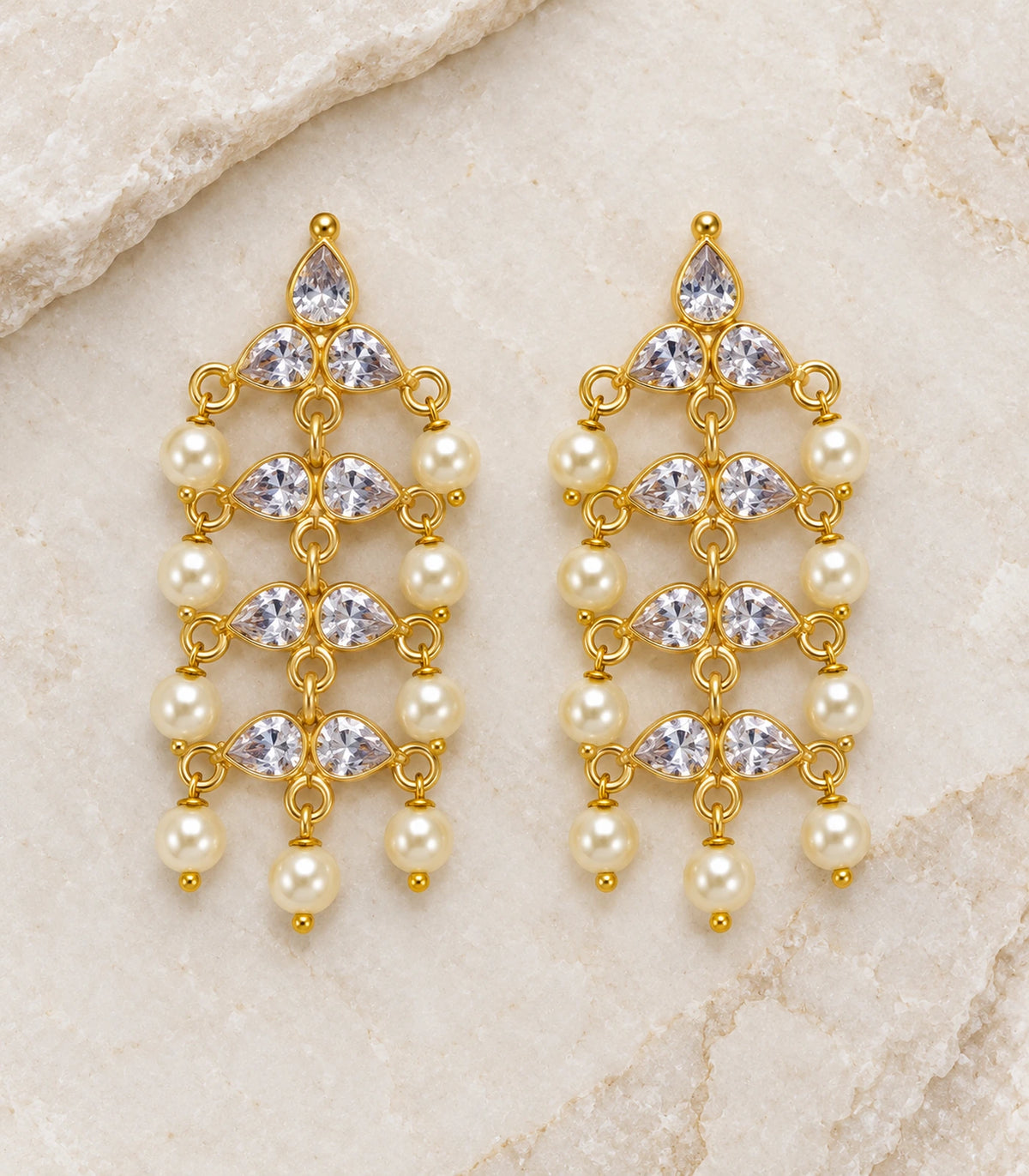 JIMIKI Gold Tone clear-crystal pearl chandelier earrings, pair arranged on a textured surface #color_gold-tone