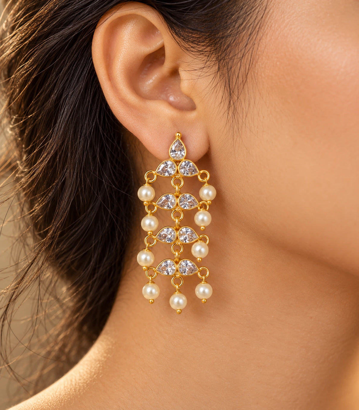 JIMIKI Gold Tone clear-crystal pearl chandelier earrings, worn in warm editorial lighting #color_gold-tone