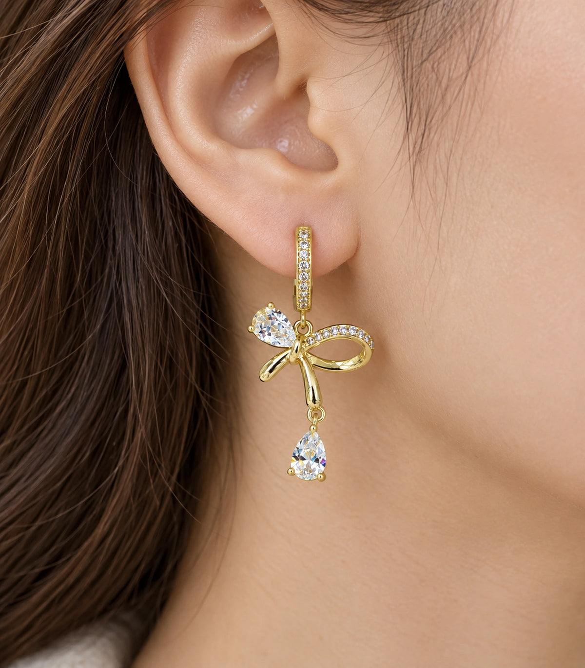 JIMIKI Gold-Tone Crystal Bow Drop Huggie Earrings in Gold / Clear, close-up detail