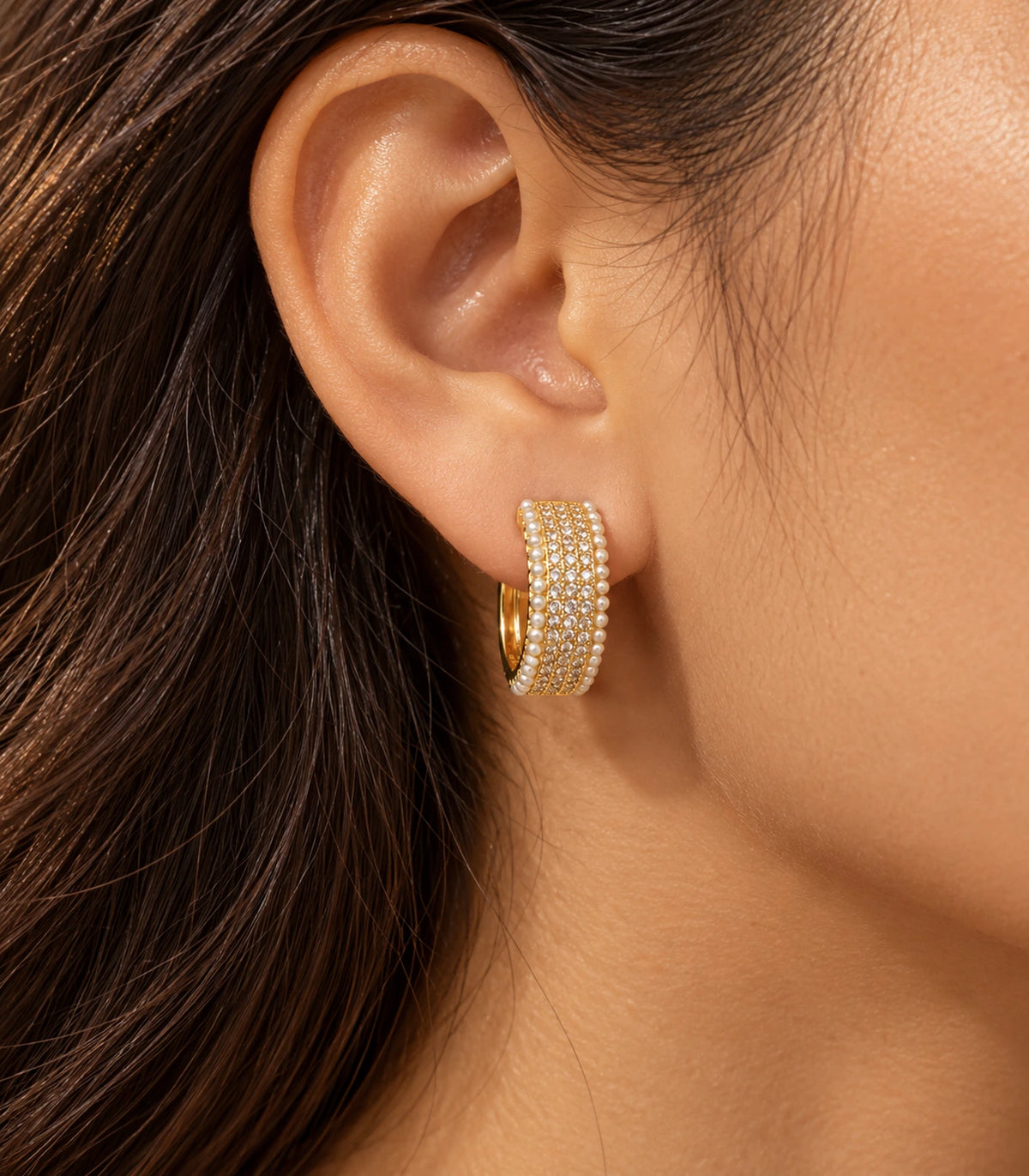 Editorial worn view of the gold-tone crystal-style and white pearl-style border huggie hoop earring