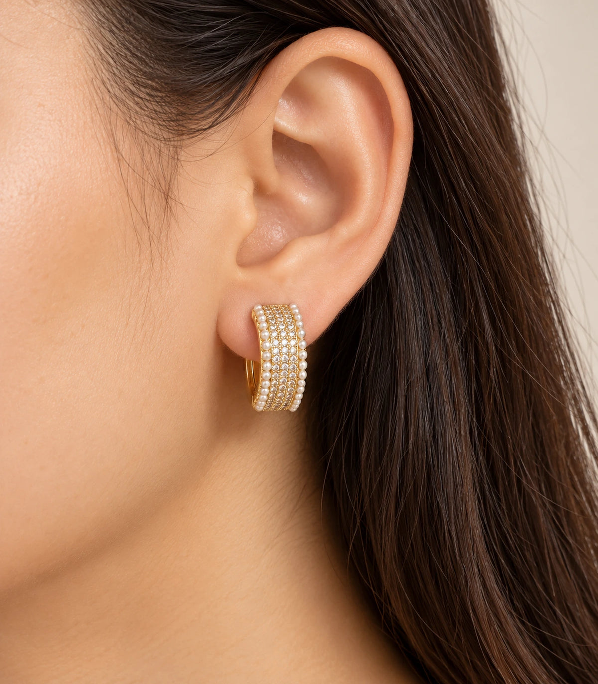 Gold-tone crystal-style and white pearl-style border huggie hoop earring worn on an ear