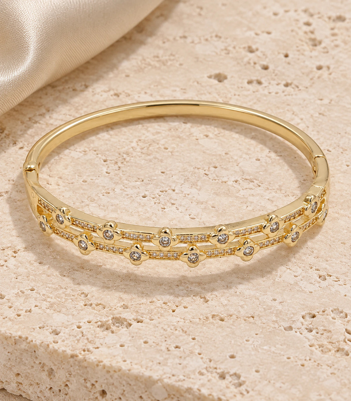 JIMIKI Gold-Tone Double Rail Bezel Crystal Bangle — bangle in a styled flat lay #color_gold-tone / clear